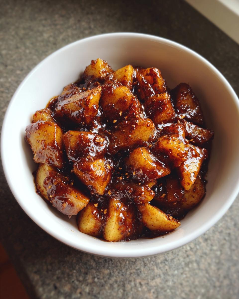 Close-up of warm, chunky Healthy Stovetop Cinnamon Apples coated in a rich, dark cinnamon glaze served in a white bowl.