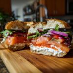 Close-up of a bagel sandwich cut in half, loaded with lox, cream cheese, lettuce, and red onion for the Build A Bagel Lunch Kit.