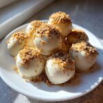 A pile of white chocolate coated Pumpkin Cheesecake Truffles topped with graham cracker crumbs on a white plate.