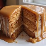 A slice removed from the Ultimate Butterscotch Cake, revealing three layers of cake and filling, generously topped with dripping butterscotch glaze.